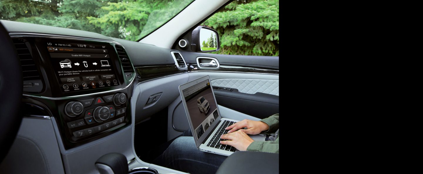 The front seat passenger using a laptop to connect to the Uconnect system in the 2020 Jeep Grand Cherokee.