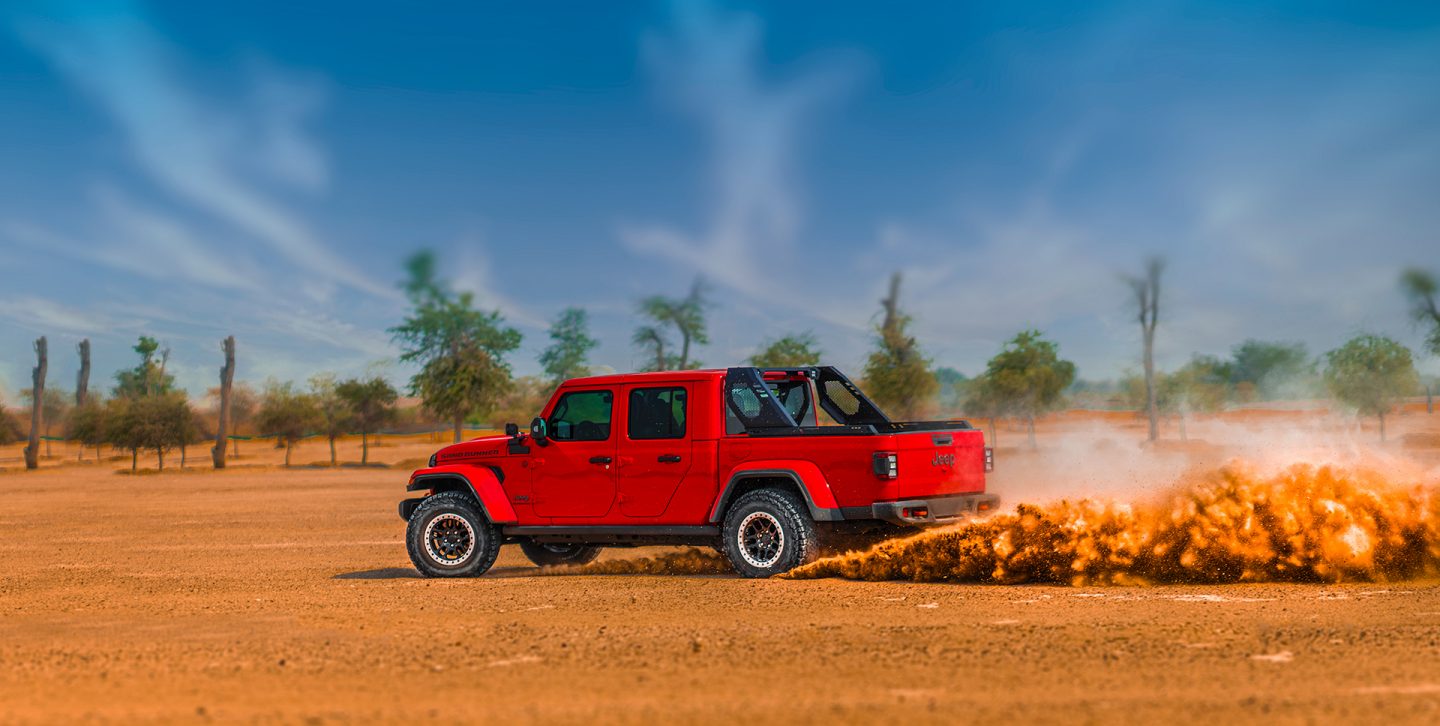 4x4 Desert Rated. The 2022 Jeep Gladiator Mojave cresting a sand dune, a cloud of dust coming from its wheels.
