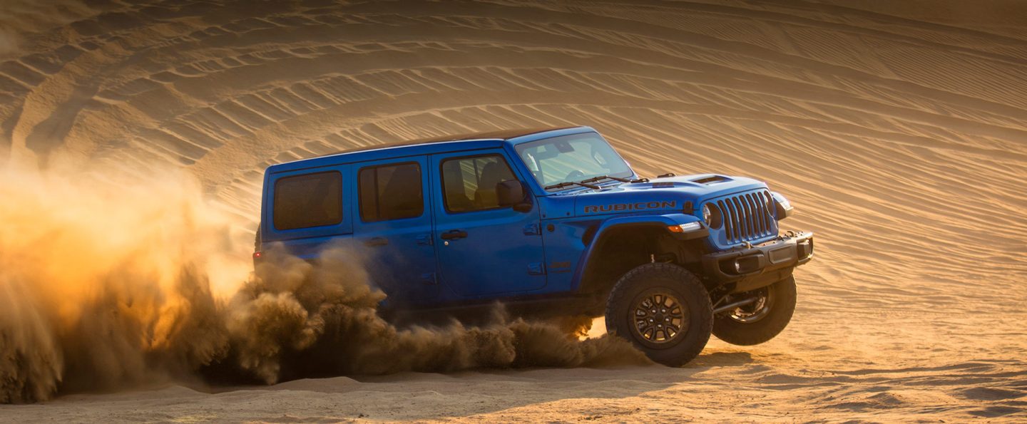 The 2022 Jeep Wrangler Rubicon 392 being driven on a sand dune, a cloud of dust coming from its wheels.