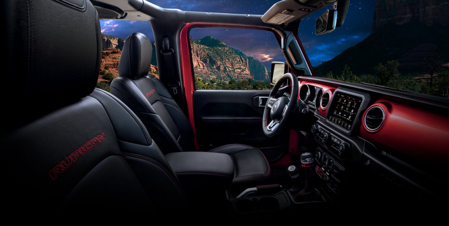 The interior of the 2022 Jeep Wrangler Rubicon, focusing on the front row, steering wheel and dashboard.