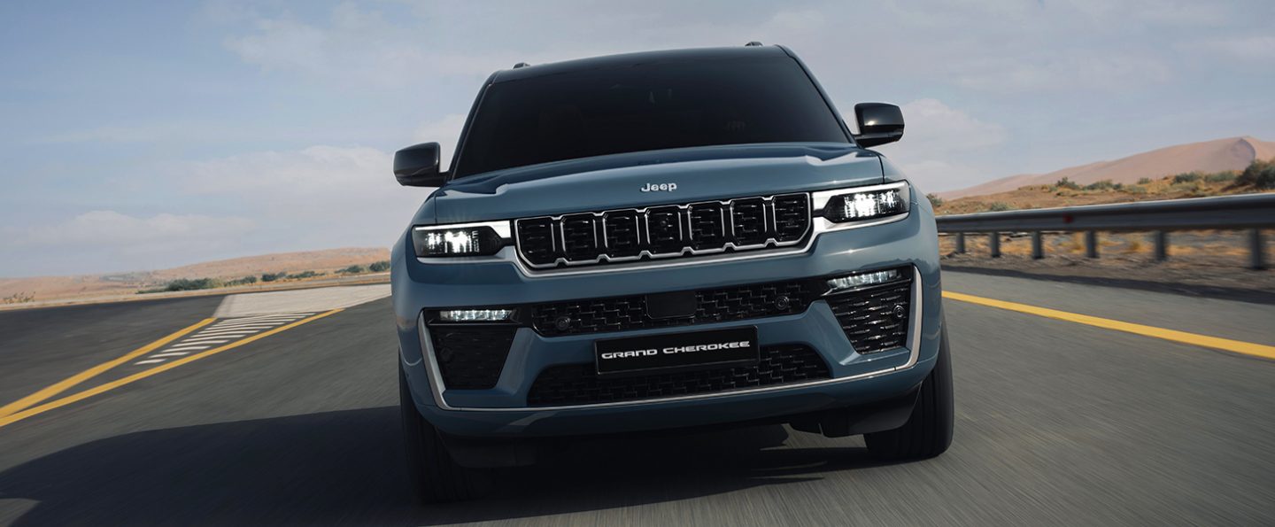 A silver 2026 Jeep Grand Cherokee Summit traveling down a highway.